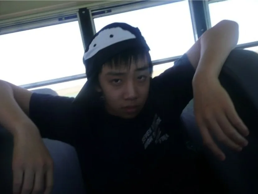 Teenage Brennan slouched across two school bus seats with his arms draped over the seat backs, wearing a backwards cap and a deadpan look.