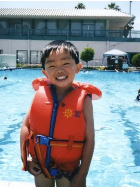 Young Brennan in an orange life jacket grinning beside a swimming pool.
